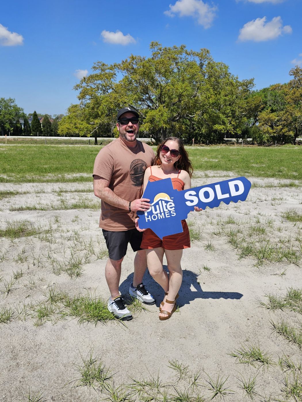 A couple holding a Pulte SOLD key on their homesite