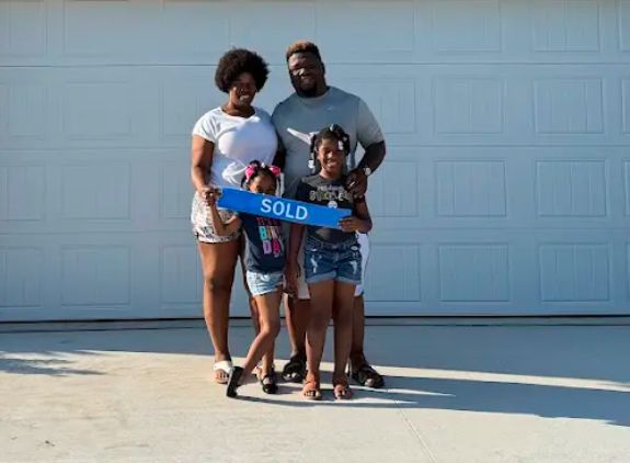A family holding a Sold sign in front of their new garage