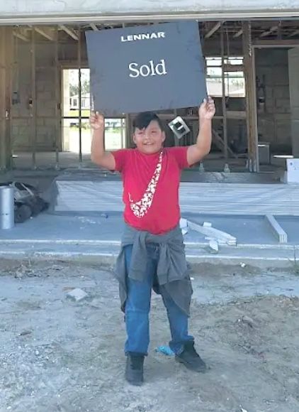 A young buyer holding up a Lennar Sold sign at the family's new home
