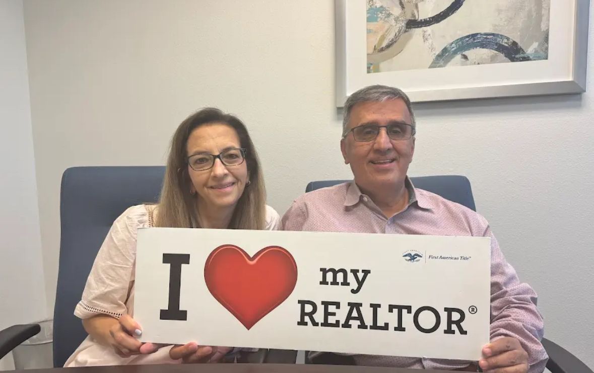 A couple holding an I love my Realtor sign at their closing