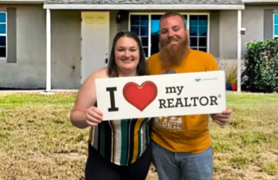 A couple holding an I love my Realtor sign in front of their home