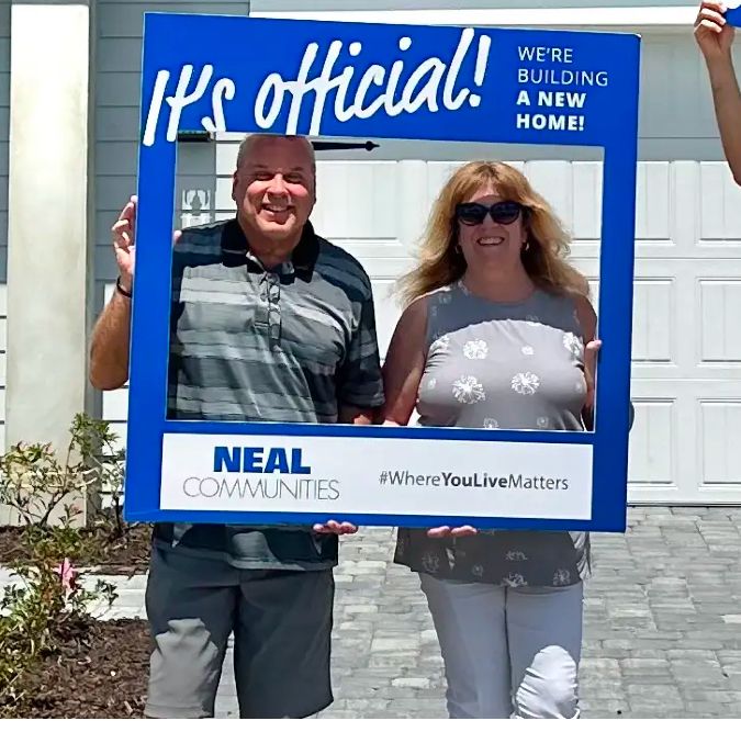 A couple holding an It's Official frame at their Neal Communities home