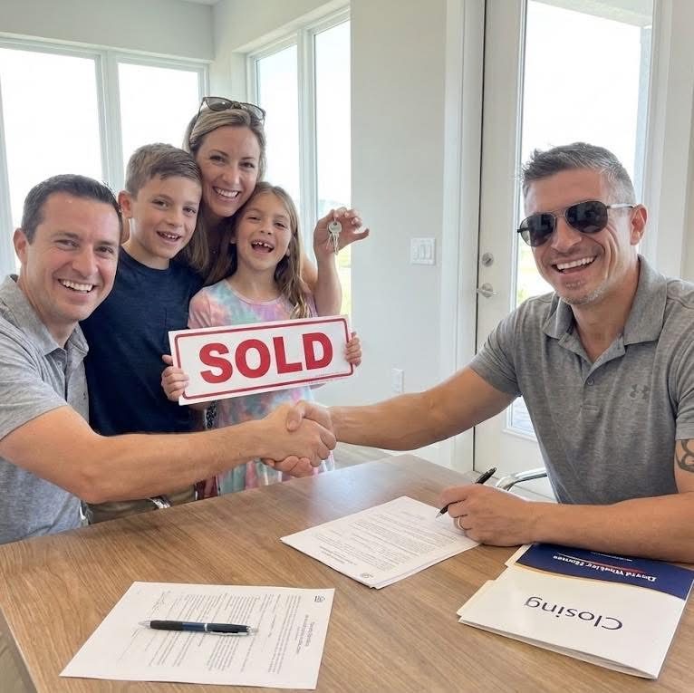 Robert Lunt shaking hands with a smiling family holding keys and a SOLD sign at their new construction closing