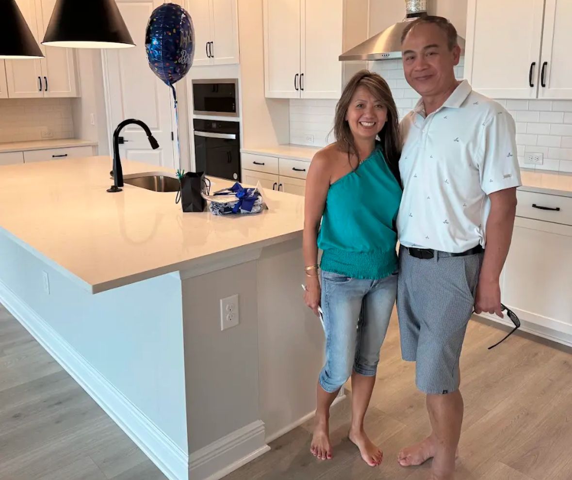 New homeowners smiling in the white kitchen of their brand-new home